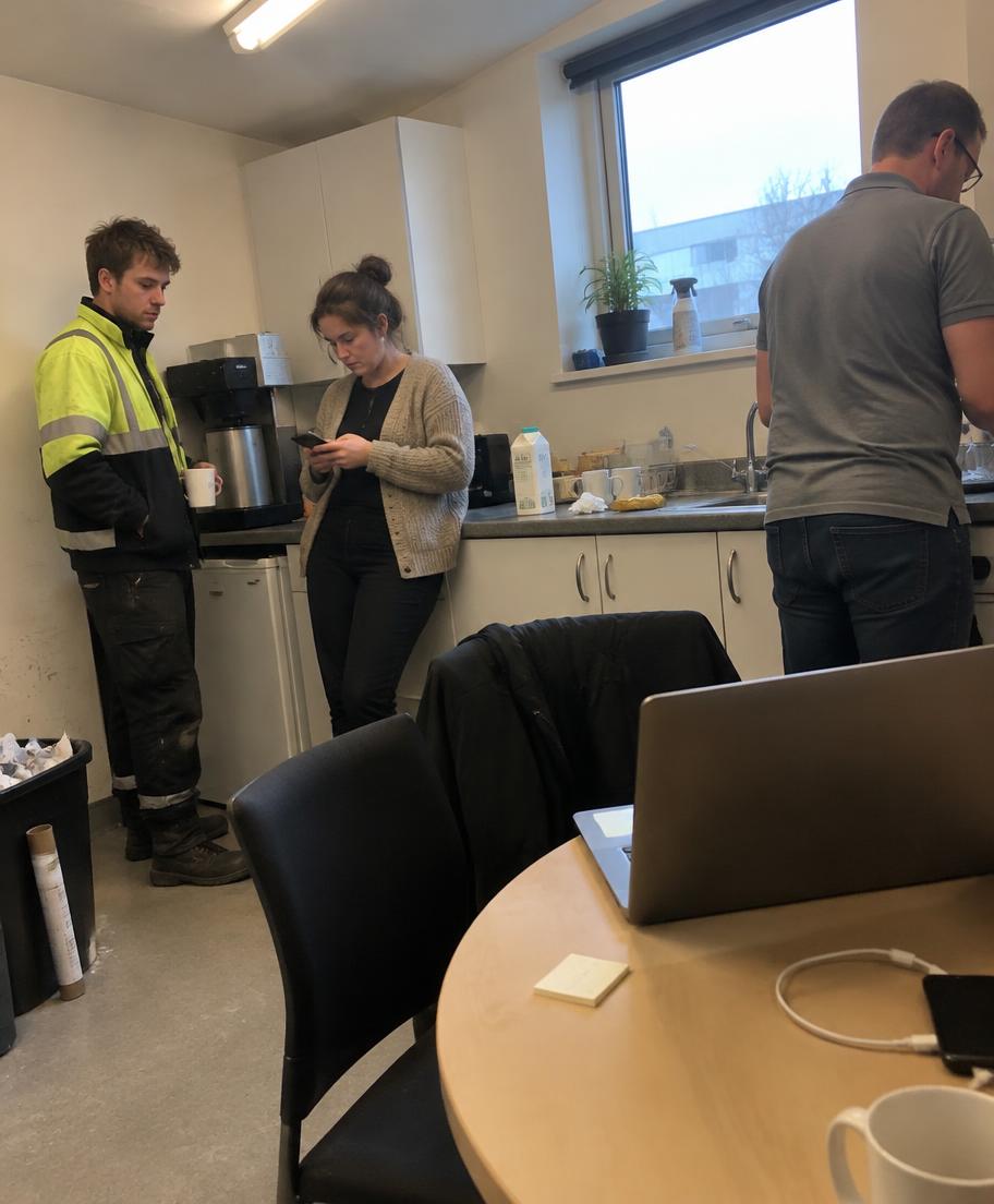 Kolleginnen und Kollegen in einer Büro-Küche, während am Tisch ein Platz leer bleibt